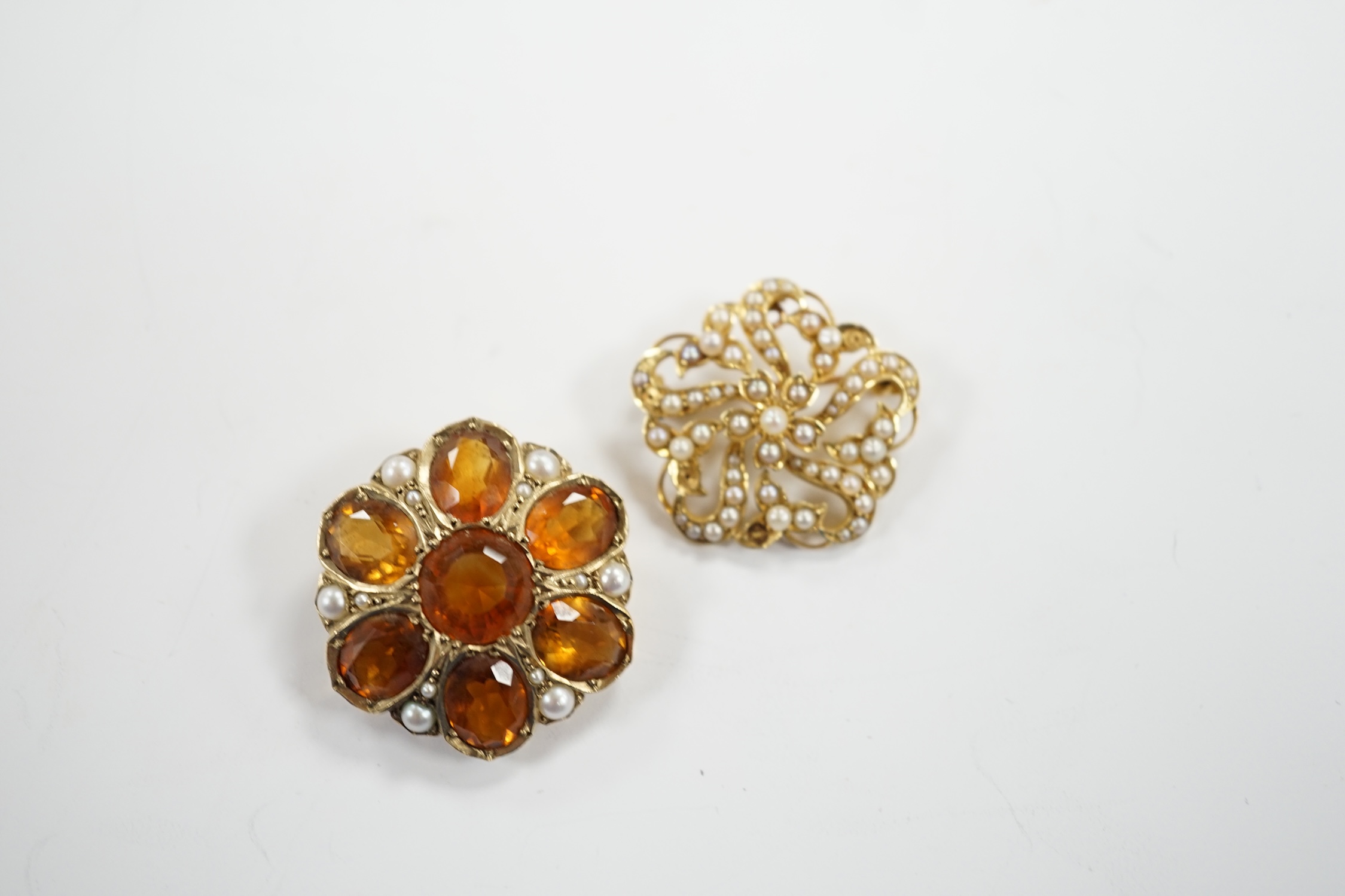 An early 20th century yellow metal, citrine and split pearl cluster set shaped circular brooch, 28mm and a similar 15ct and seed pearl cluster set brooch, gross weight 18.5 grams.